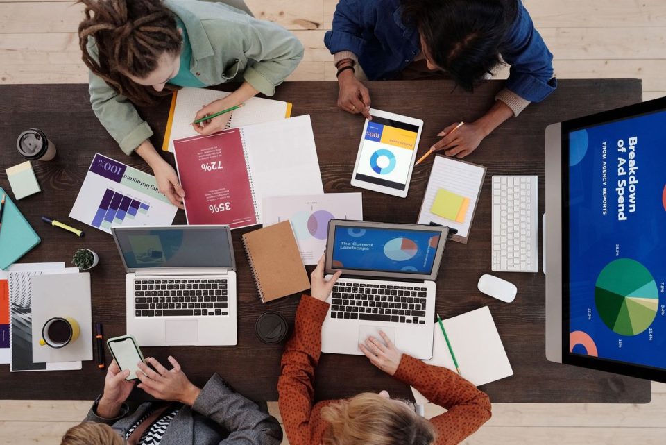 Equipe diversa de profissionais colaborando em uma mesa, usando laptops e tablets para discutir estratégias de marketing digital.