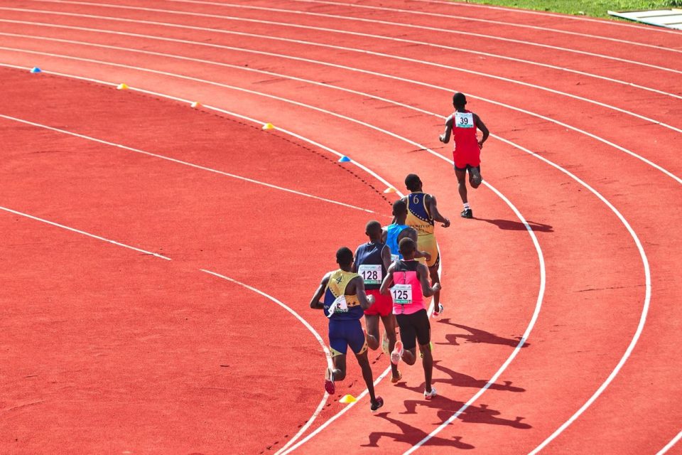 Atletas disputam uma corrida em pista curva ao ar livre.