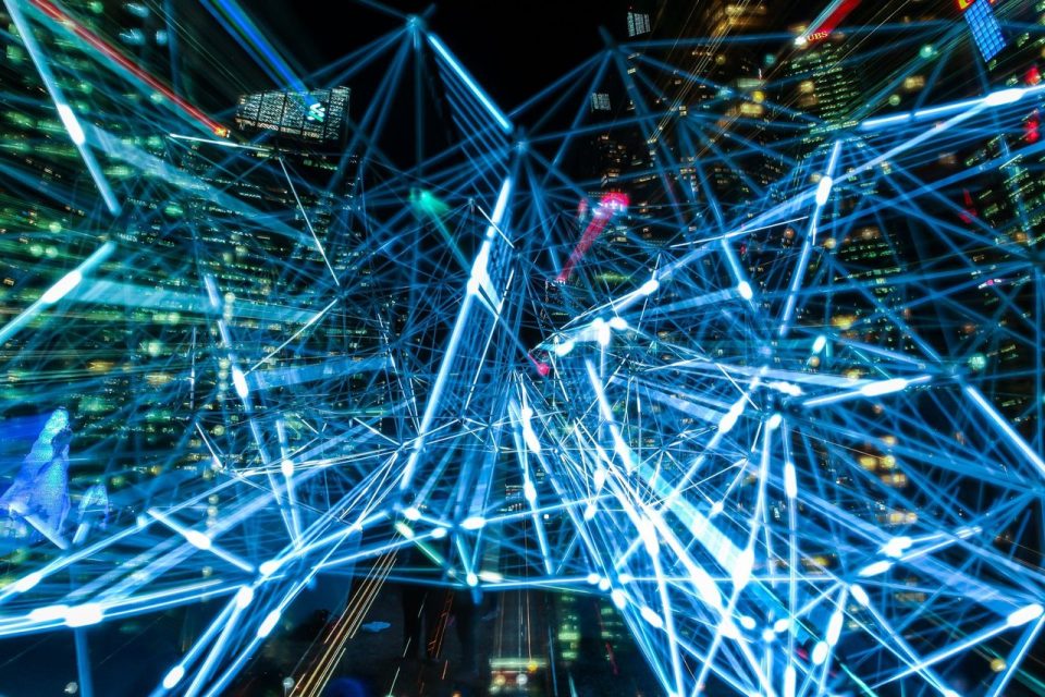 Cena urbana noturna com trilhas luminosas interconectadas, simbolizando uma rede de comunicação digital.