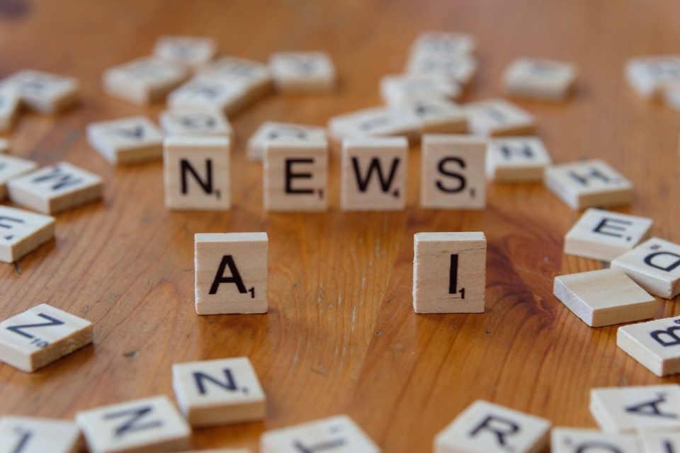 Peças de Scrabble formam as palavras “AI” e “NEWS” sobre uma superfície de madeira.