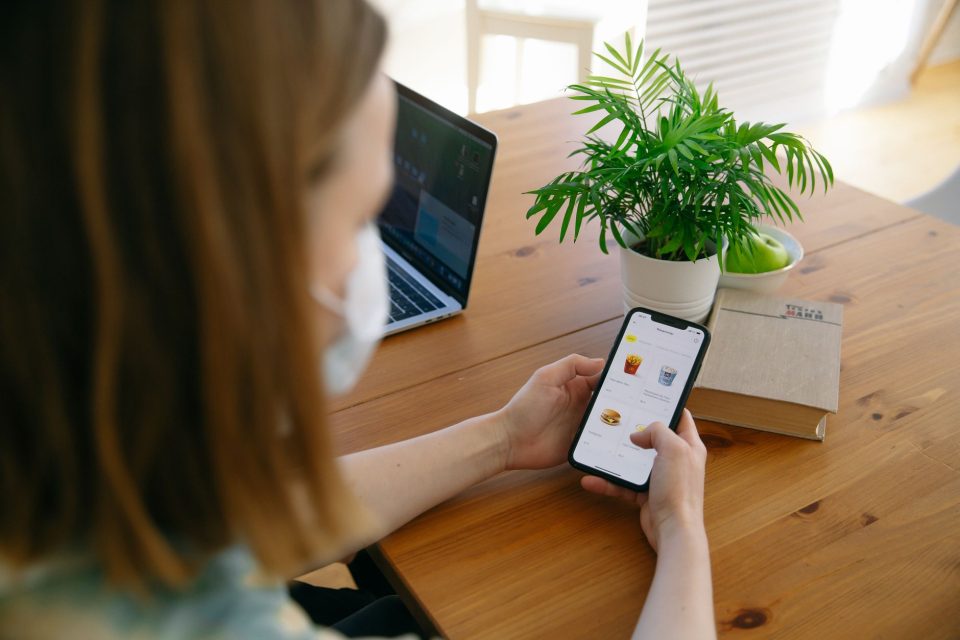 Mulher usando um smartphone ao lado de um laptop durante uma compra online em ambiente doméstico.